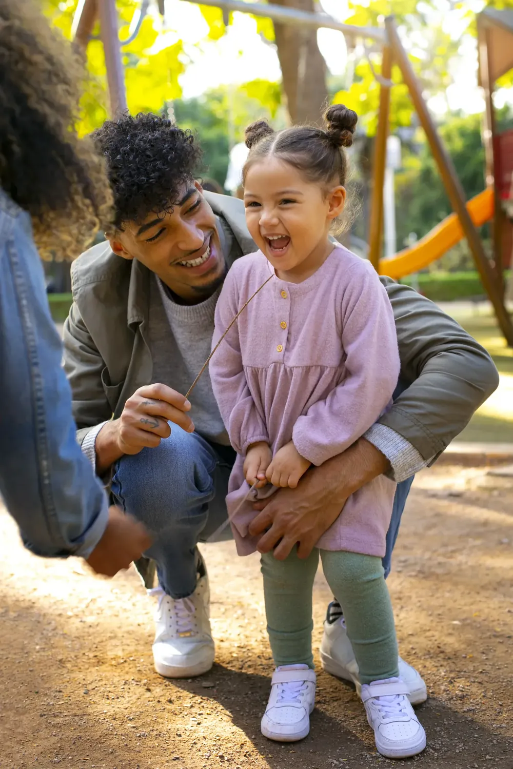 Father kneeling beside his laughing young daughter at a playground